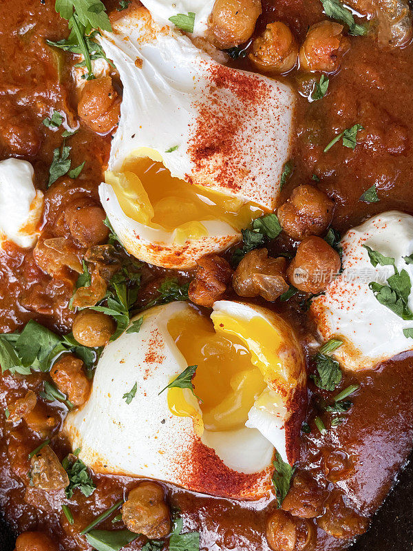 地中海健康早餐的全画幅图片:shakshouka / shakshuka / chakchouka，鹰嘴豆，鸡蛋在番茄，辣椒，洋葱，橄榄油和大蒜的酱汁中水煮，顶部有香菜，高架视图